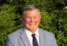 Smiling man in suit with greenery background.