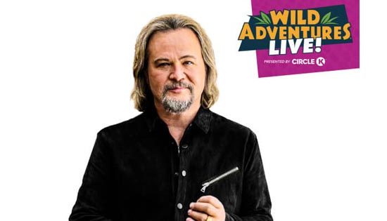 Man with gray hair beside Wild Adventures poster