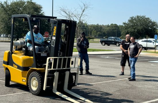 Yellow forklift with people observing in parking lot